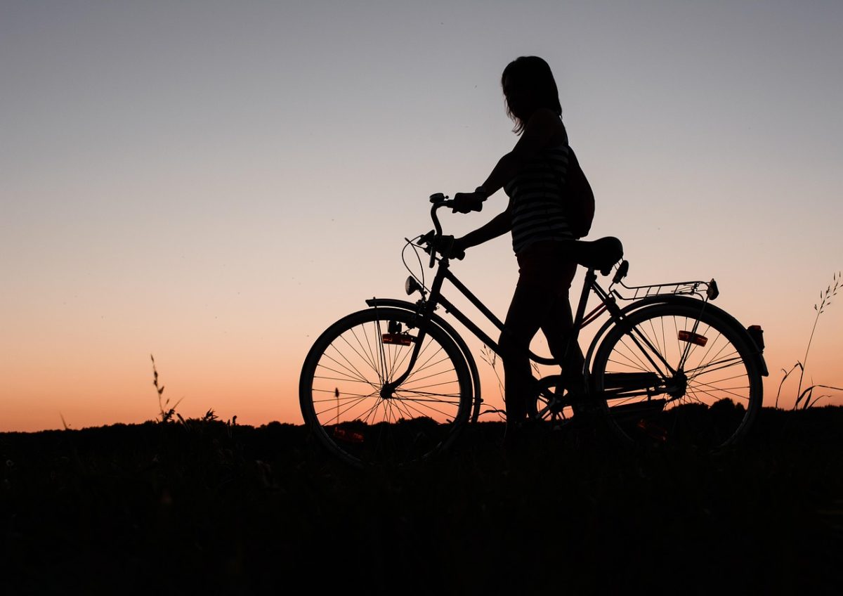Silhouette d’une jeune femme marchant à côté de son vélo dans la nature au coucher du soleil