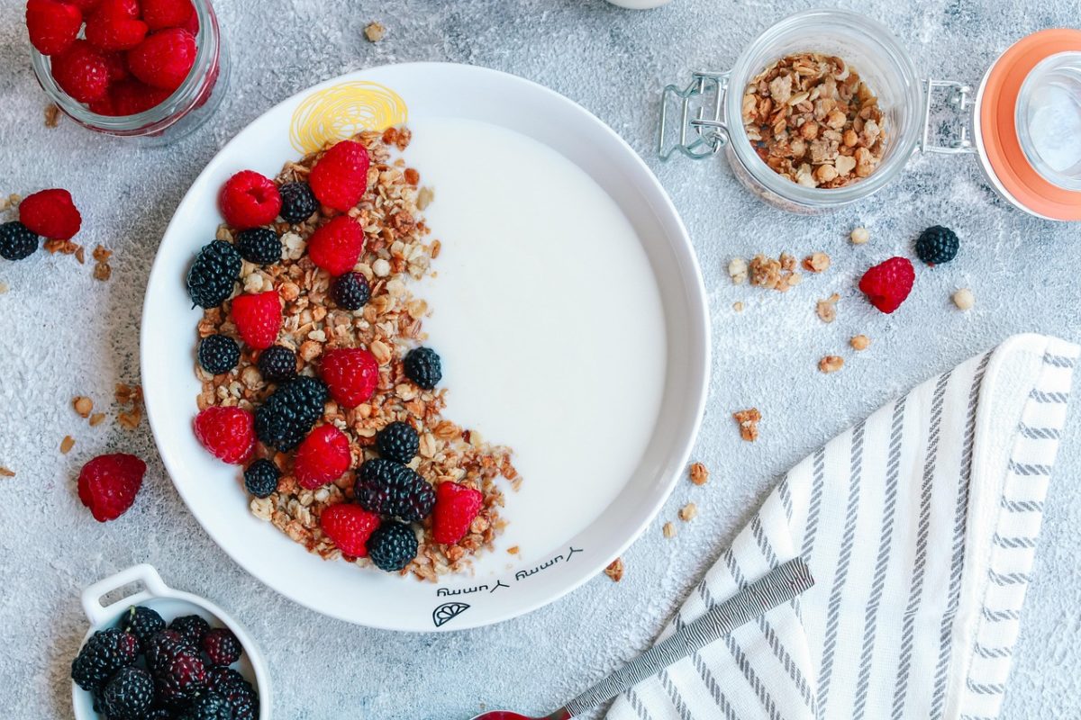 Bol de yaourt avec des granolas, des framboises et des mûres. Avec à coté des minis pots de fruits rouges et de granolas ainsi qu’une serviette rayée en tissu.