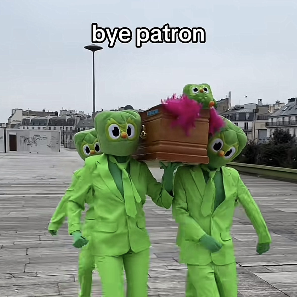 uatre personnes déguisées en hibou Duo transportent un cercueil en bois dans la rue. Le texte “bye patron” renforce le ton humoristique et absurde de la scène.