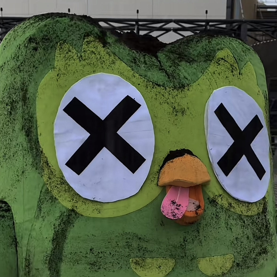 la mascotte Duolingo est représentée avec des yeux en croix, la langue pendante et de la terre sur lui, parodiant une scène de mort cartoon.